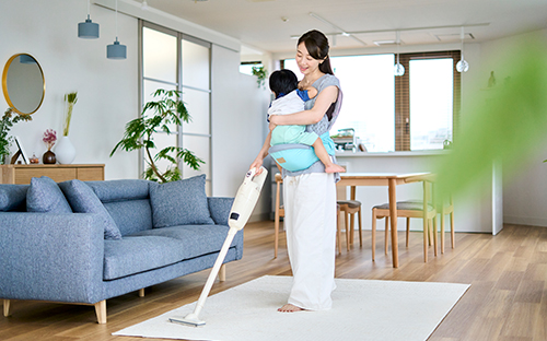子供を抱きかかえながら部屋の掃除機をかける女性